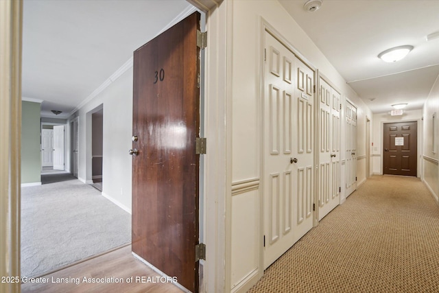 corridor featuring light carpet, baseboards, and ornamental molding