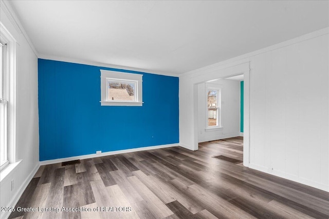 spare room featuring crown molding, wood finished floors, visible vents, and baseboards