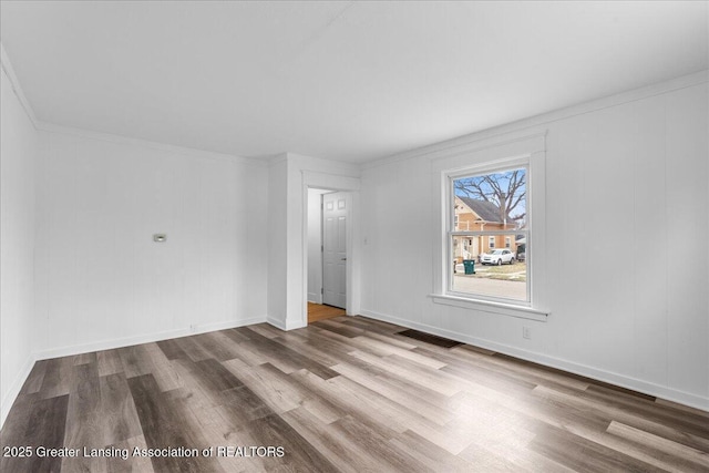 unfurnished room with crown molding, wood finished floors, visible vents, and baseboards