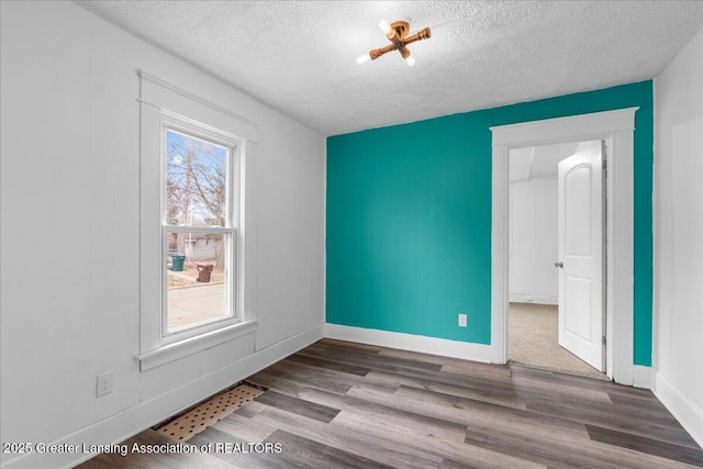 unfurnished room featuring a textured ceiling, baseboards, and wood finished floors