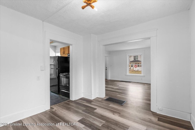 spare room featuring dark wood-type flooring, visible vents, a textured ceiling, and baseboards