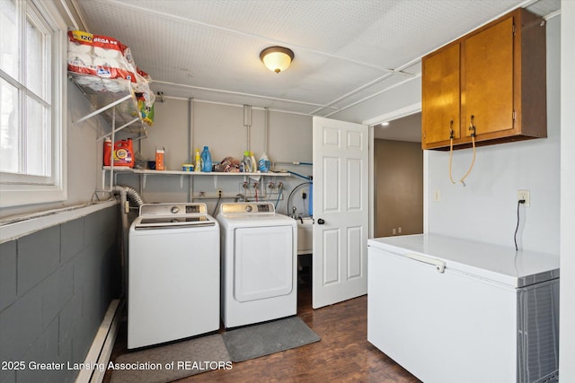 washroom with concrete block wall, dark wood finished floors, washer and clothes dryer, a baseboard radiator, and cabinet space