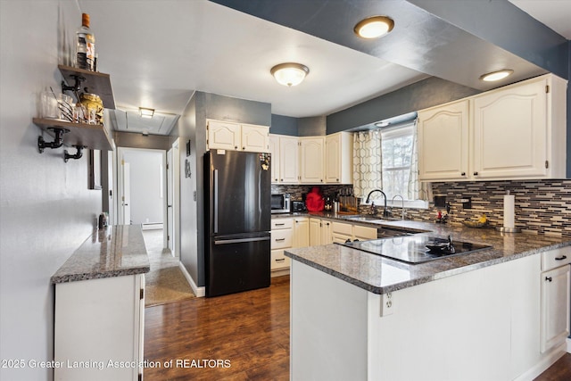 kitchen featuring black electric stovetop, dark wood-type flooring, freestanding refrigerator, a sink, and a peninsula