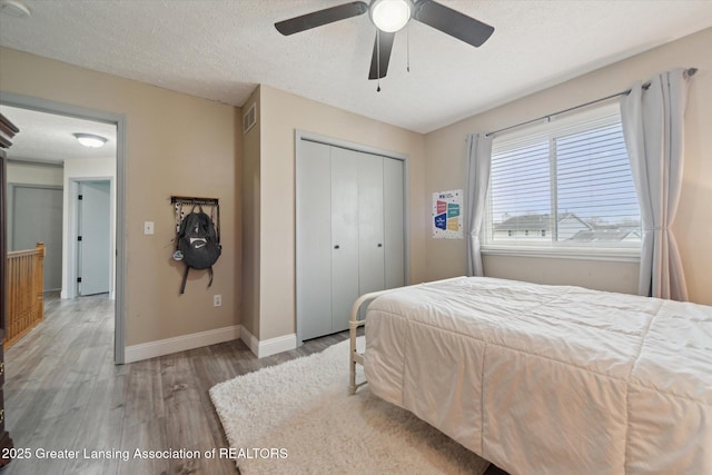 bedroom featuring light wood finished floors, baseboards, visible vents, a textured ceiling, and a closet