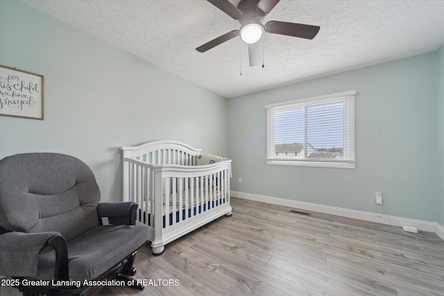 bedroom featuring a crib, visible vents, baseboards, and wood finished floors