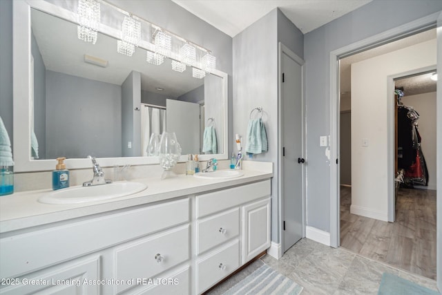 full bath with double vanity, a spacious closet, a sink, and baseboards