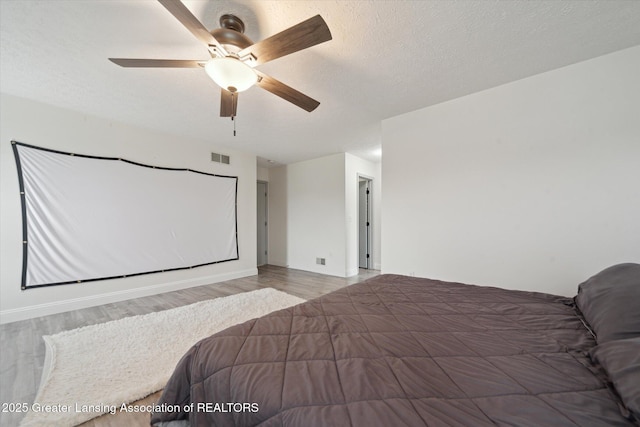 bedroom featuring ceiling fan, visible vents, a textured ceiling, and wood finished floors