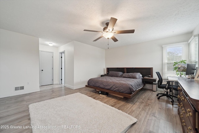 bedroom with a textured ceiling, wood finished floors, a ceiling fan, visible vents, and baseboards