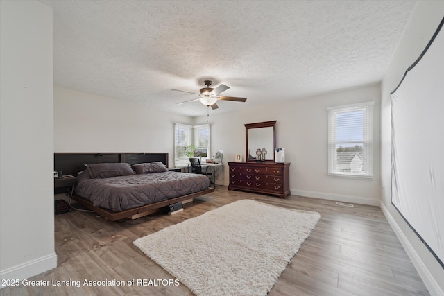 bedroom featuring light wood-type flooring, ceiling fan, baseboards, and a textured ceiling