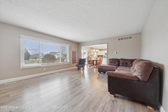 living area with a chandelier, light wood-type flooring, visible vents, and baseboards