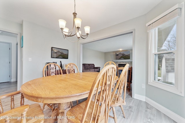 dining area featuring a notable chandelier, light wood finished floors, a fireplace, and baseboards