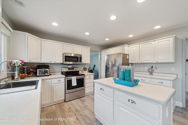 kitchen featuring light wood finished floors, white cabinetry, appliances with stainless steel finishes, and a sink