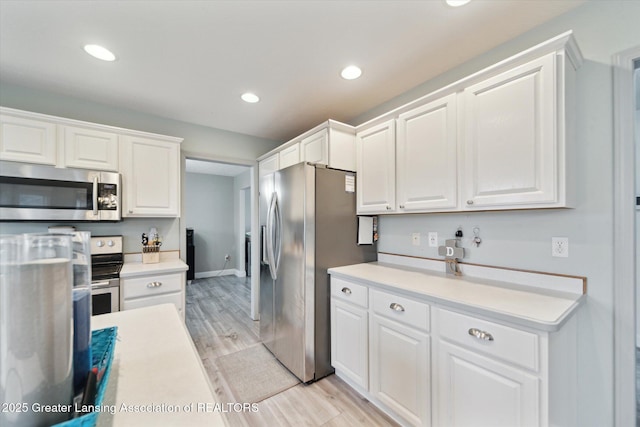 kitchen with appliances with stainless steel finishes, light countertops, white cabinets, and light wood-style floors