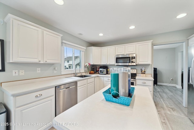 kitchen with stainless steel appliances, light countertops, a sink, and white cabinetry