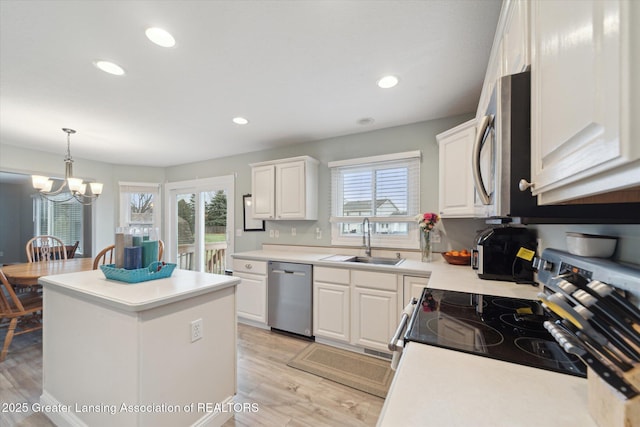 kitchen with light wood finished floors, appliances with stainless steel finishes, a center island, white cabinetry, and a sink