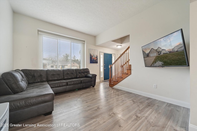 living room featuring a textured ceiling, stairway, wood finished floors, and baseboards