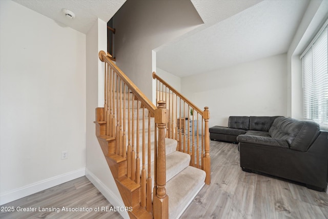 stairs with a textured ceiling, baseboards, and wood finished floors