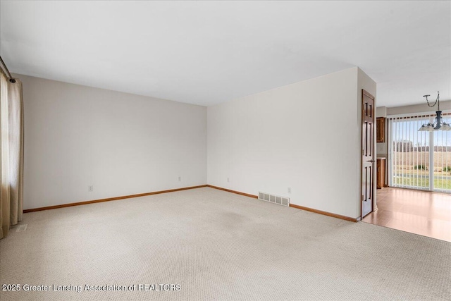 unfurnished room with light carpet, a notable chandelier, visible vents, and baseboards