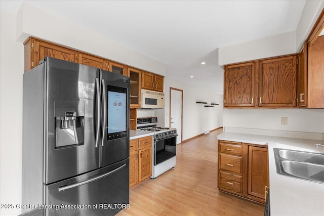 kitchen featuring light countertops, brown cabinetry, a sink, light wood-type flooring, and white appliances