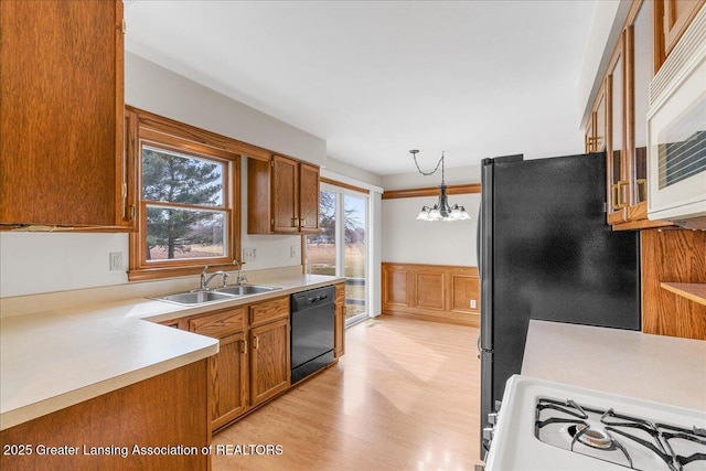 kitchen featuring light wood-style flooring, brown cabinets, light countertops, black appliances, and a sink