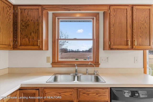 kitchen featuring dishwashing machine, brown cabinetry, a sink, and light countertops