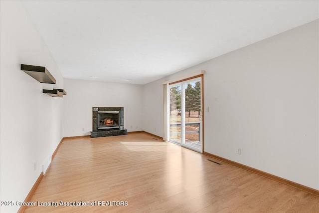 unfurnished living room with light wood finished floors, a fireplace, visible vents, and baseboards