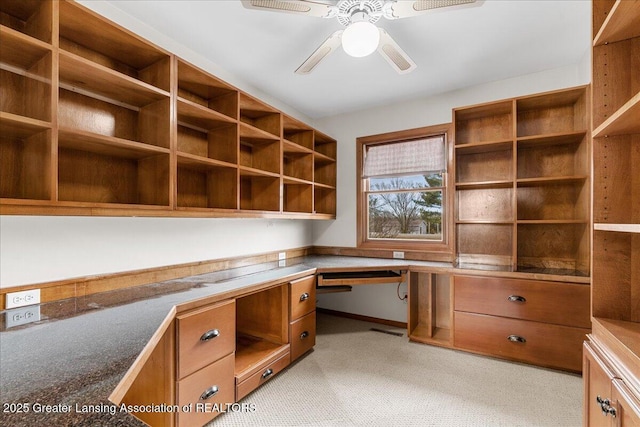 unfurnished office with light carpet, a ceiling fan, and built in desk