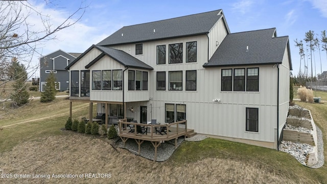 back of house with a shingled roof, a deck, a lawn, and a sunroom