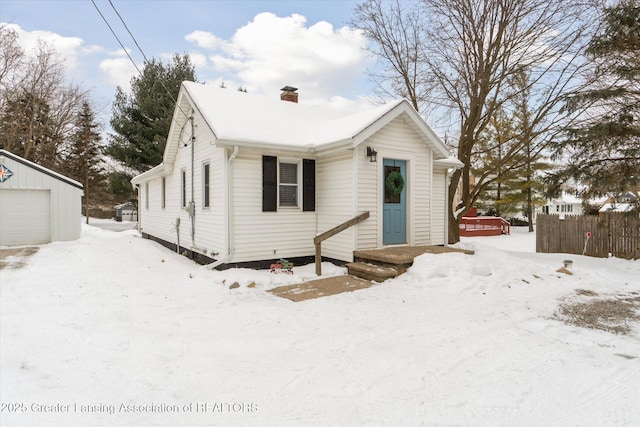 view of front of home featuring an outbuilding, a chimney, a detached garage, and fence