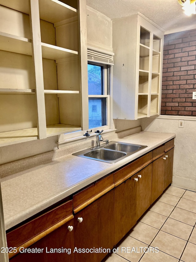 kitchen featuring light tile patterned floors, light countertops, a sink, a textured ceiling, and brick wall