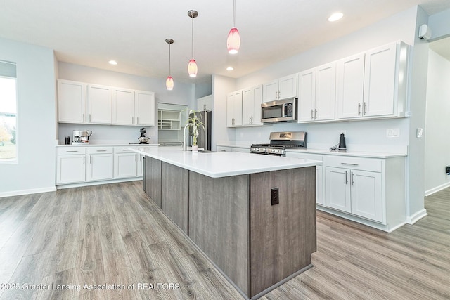 kitchen featuring light wood finished floors, stainless steel appliances, light countertops, white cabinets, and a sink