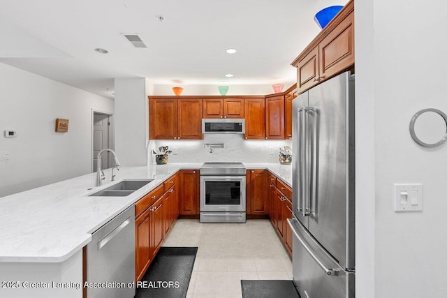 kitchen with visible vents, appliances with stainless steel finishes, brown cabinetry, a sink, and a peninsula