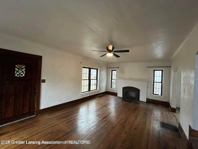 unfurnished living room with baseboards, visible vents, a ceiling fan, dark wood-style flooring, and a fireplace