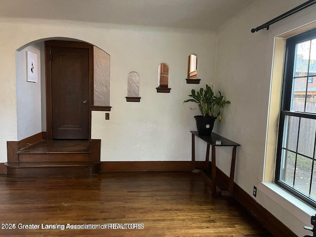 corridor featuring arched walkways, baseboards, and wood finished floors