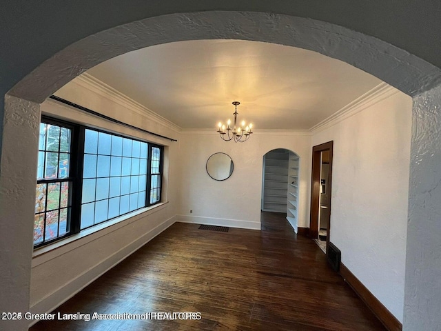 spare room with ornamental molding, a notable chandelier, baseboards, and wood finished floors