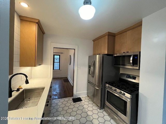 kitchen with baseboards, decorative backsplash, appliances with stainless steel finishes, light stone countertops, and a sink