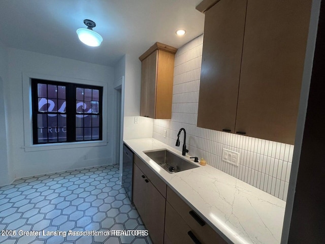 kitchen with black dishwasher, light stone counters, a sink, and decorative backsplash