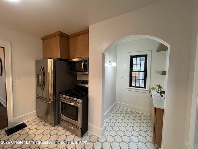 kitchen with arched walkways, appliances with stainless steel finishes, visible vents, and baseboards