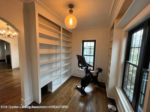 workout area featuring baseboards, arched walkways, dark wood-style floors, crown molding, and built in shelves