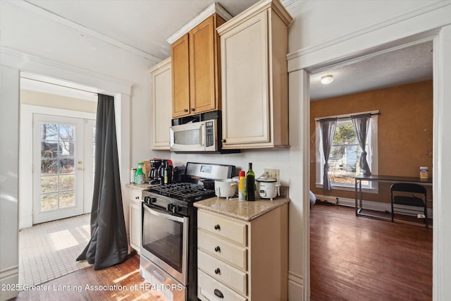 kitchen featuring baseboards, stainless steel gas range oven, wood finished floors, and light stone countertops