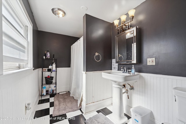 full bath featuring a shower with shower curtain, tile patterned floors, and wainscoting