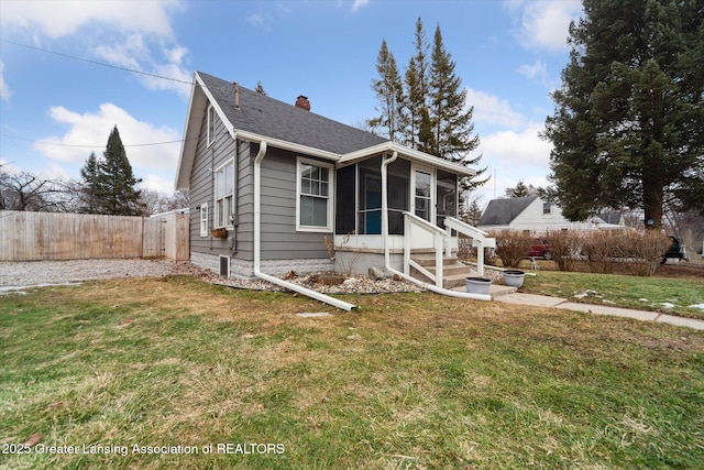 bungalow-style house with a sunroom, fence, a chimney, and a front lawn