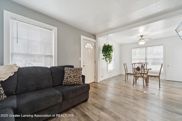 living area with a ceiling fan, visible vents, baseboards, and wood finished floors