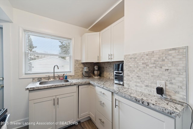 kitchen featuring light stone countertops, tasteful backsplash, white cabinets, and a sink