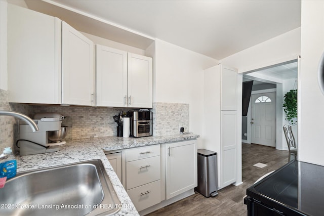 kitchen with a sink, light stone countertops, black range with electric cooktop, white cabinetry, and backsplash