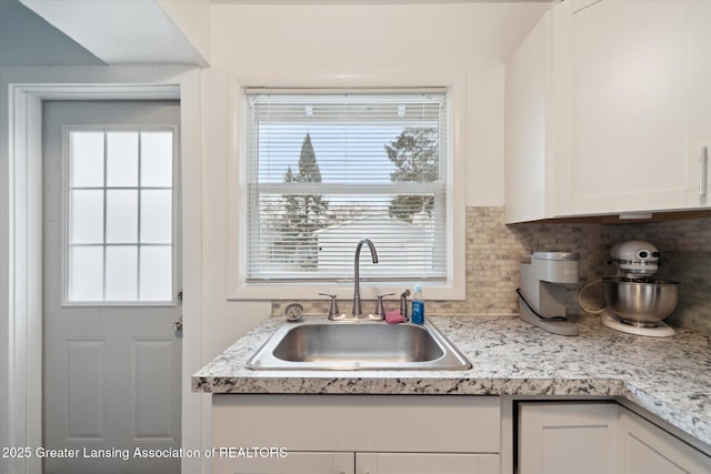 kitchen featuring tasteful backsplash, light countertops, white cabinetry, and a sink