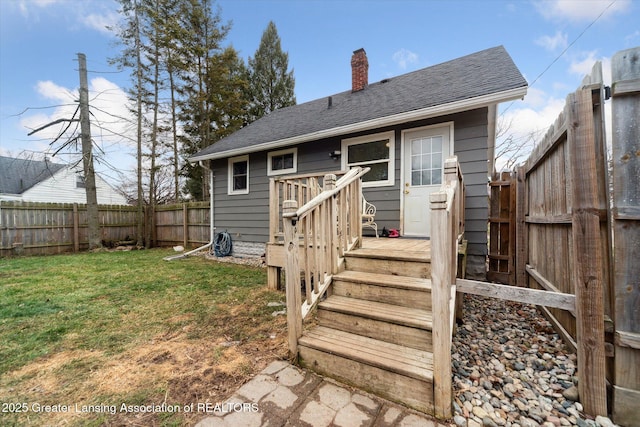 back of property with a fenced backyard, a chimney, roof with shingles, a yard, and a wooden deck