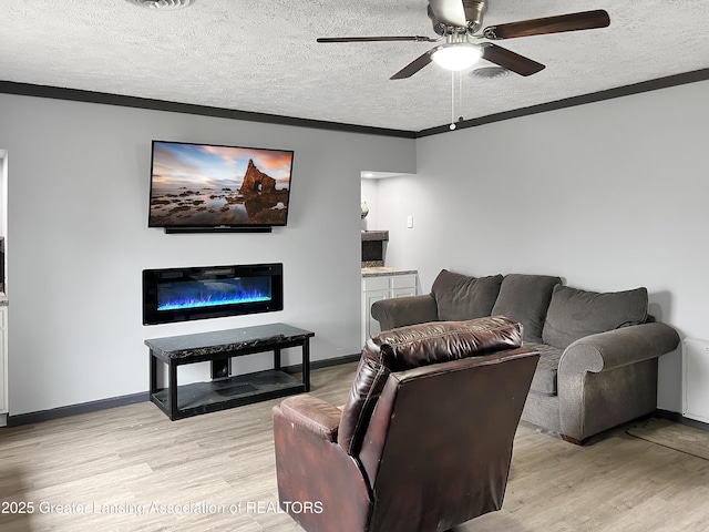 living room featuring baseboards, a glass covered fireplace, light wood-style flooring, a textured ceiling, and crown molding