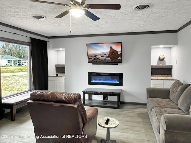 living room with a textured ceiling, visible vents, crown molding, and a glass covered fireplace