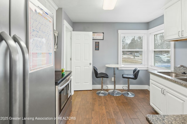 kitchen featuring dark wood-style flooring, appliances with stainless steel finishes, white cabinets, a sink, and baseboards